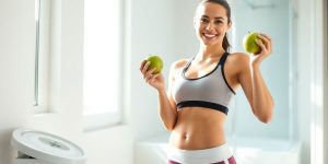 Woman smiling, holding apple, standing by scale.